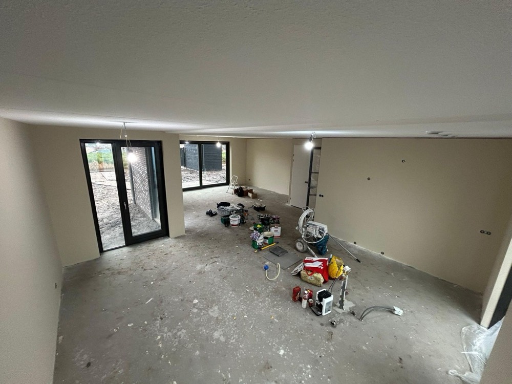 Woonkamer van een nieuwbouwwoning tijdens het spuitwerk, met airless spuitmachine